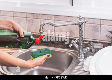 Frau mit roten Maniküre, Reinigungsmittel im topfreiniger, das Geschirr zu waschen. Stockfoto