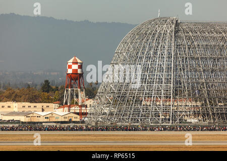 Eine große Menschenmenge steht vor dem Hangar One von Moffett Field und dem berühmten Wasserturm und wartet wahrscheinlich darauf, den Hangar für eine Veranstaltung oder Tour zu betreten. Stockfoto