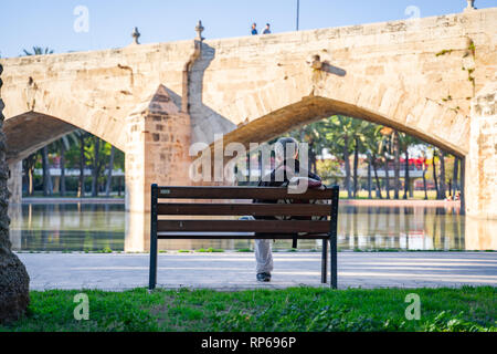 Valencia, Spanien - 16. Februar 2019: Mann auf der Bank sitzen und das Buch zu lesen. Mittelalterliche Brücke. Stockfoto