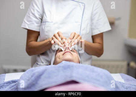 Junge Frau liegend auf Massage Schreibtisch genießen eine Hautpflege Behandlung als Kosmetiker reinigt Ihr Gesicht mit Wattepads. Stockfoto