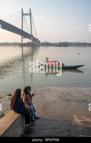 Ein Blick auf die vidyasagar Setu Brücke aus Das Prinsep Ghat, die auf dem Hooghly River bei Sonnenuntergang mit einem touristenboot und Einheimischen in den Vordergrund. Stockfoto