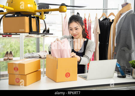 Junge asiatische Frauen packen Tuch auf Box für Lieferung an Kunden von Air Drone, kleine Unternehmen mit moderner Technik Versand Innovation und Eco-Konzept Stockfoto