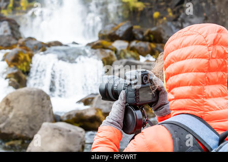 Nationalpark Thingvellir, Island Oxararfoss Wasserfall felsige Landschaft auf Golden Circle mit Wasser Fluss und touristische Frau in orange Jacke pi nehmen Stockfoto