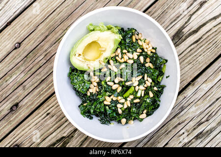 Flache Ansicht von Kale green vegan vegetarisch Salat auf hölzernen Picknicktisch mit Pinienkernen und Avocado Hälfte in der Schüssel Stockfoto