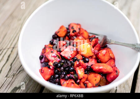 Nahaufnahme von Lila Rot mango Obst Heidelbeeren vegan vegetarisch Salat auf hölzernen Picknicktisch mit Gabel in der Schüssel und orange leuchtende Farben Stockfoto