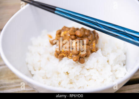 Nahaufnahme des blauen Stäbchen auf Asiatisch Japanisch natto fermentierte Soja dish Meal klebrige schleimigen Textur in schlichtem Weiß gedämpftem Reis in der Schüssel Stockfoto