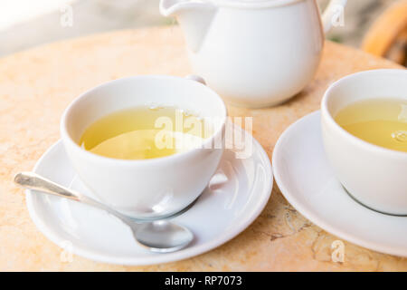 Nahaufnahme von zwei weiße Tassen auf Teller untertassen von Grünen oder oolong Tee beim Frühstück Brunch im Cafe Restaurant außerhalb Tabelle mit Teekanne pot Stockfoto