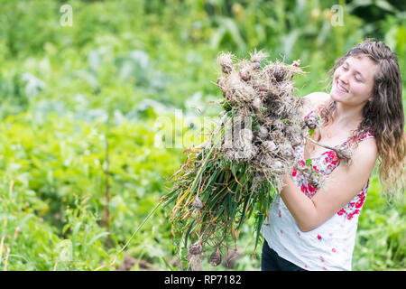 Junge Frau Mädchen Bauern ernten Knoblauch Zwiebeln in Hof oder Garten holding Bündel Gemüse glücklich lächelnde closeup Stockfoto