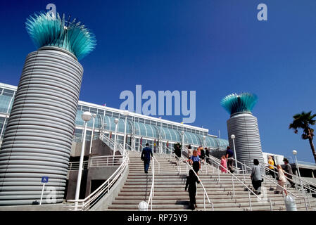 Konferenzteilnehmer ascend breiten Stufen hinter ein paar zeitgenössische Glasablage spalten das Long Beach Convention Center, die entlang der Downtown waterfront von Long Beach, Kalifornien, USA. Das beeindruckende Gebäude Glasfassade ermöglicht viel Sonnenschein in Hallen- und Tagungsräume, die Teil einer Convention-, Entertainment, das auch zwei Theater und eine Arena für Konzerte und Sportveranstaltungen. Stockfoto