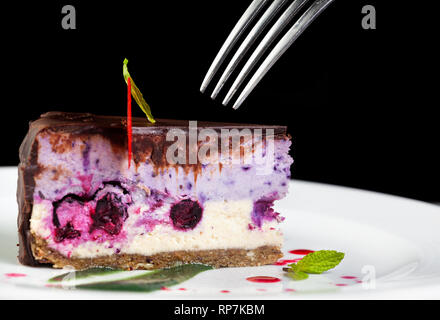 Raw vegan Kuchen mit Beeren von Küchenchef auf weißen Teller dekoriert mit Gabel im Restaurant auf schwarzem Hintergrund Stockfoto