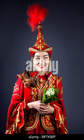 Frau in Rot nationalen kasachischen Kostüm holding Blumenstrauß Blume an grauer Hintergrund Stockfoto