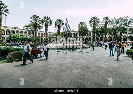 Street Scene von Parque Central in Arequipa (Peru) mit Einheimischen, Tauben, Palmen und kolonialen Gebäuden. Stockfoto