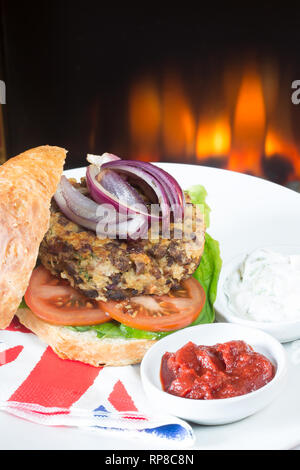 Hausgemachte Quorn Burger in einem sauerteig Brötchen mit Salat, Tomaten, roten Zwiebeln, serviert mit Ketchup und Soja Joghurt Dips. Stockfoto