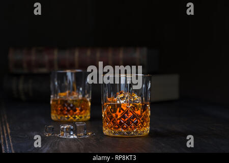 Whiskey zwei Gläser mit Eis, stand auf einem dunklen alten Holztisch mit alten Büchern auf schwarzem Hintergrund