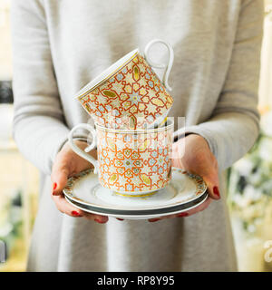 Elegante Tee oder Kaffee Tassen und Untertassen in Frauenhand. Frau hält eine keramische Schüssel. Stockfoto