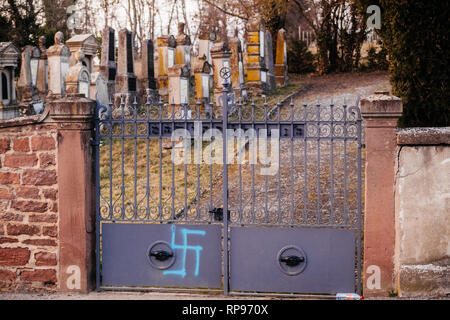 Eingangstor mit Blau spray Swastika Zeichen und zerstörte Gräber mit NS-Symbolen in blau Spray - auf den beschädigten Gräber - Jüdischer Friedhof in Quatzenheim in der Nähe von Straßburg gestrichen. Stockfoto