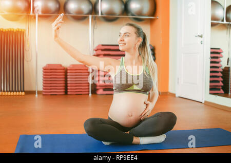 Yoga für schwangere Frauen. Junge schöne schwangere Mädchen im Lotussitz sitzen und selfie Stockfoto