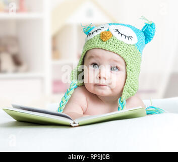 Baby infany in lustige Eule Strickmütze Eule liegend mit Buch im Kindergarten Stockfoto