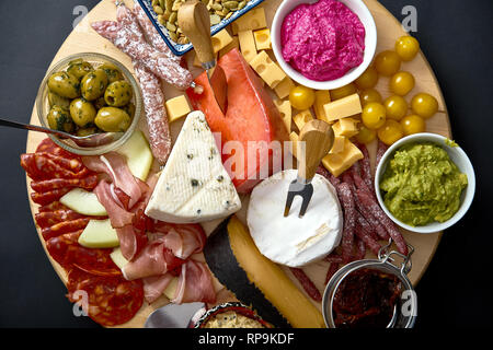 Antipasti board mit verschiedenen Käse und Fleisch Snacks mit Hummus und Oliven auf Holz- runde Board auf schwarz Tabelle Stockfoto