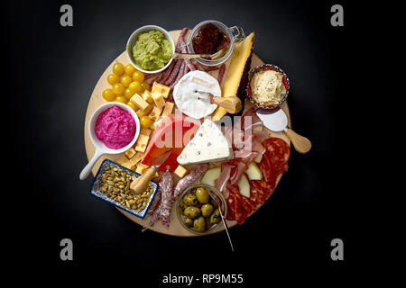 Antipasti board mit verschiedenen Käse und Fleisch Snacks mit Hummus und Oliven auf Holz- runde Board auf schwarz Tabelle Stockfoto