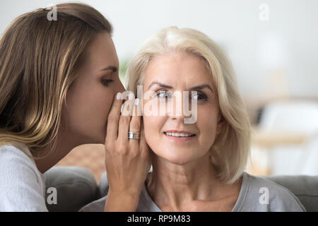 Junge Frau whispering gute Nachrichten, Geheimnis in betagte Mutter, Ohr Stockfoto