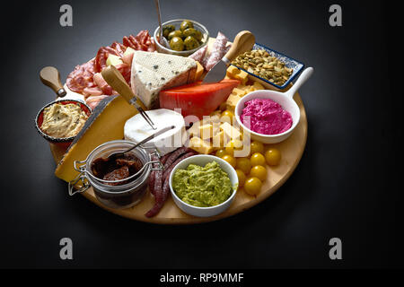 Antipasti board mit verschiedenen Käse und Fleisch Snacks mit Hummus und Oliven auf Holz- runde Board auf schwarz Tabelle Stockfoto