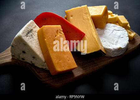 Holzbrett mit verschiedenen Arten von Käse auf schwarzem glatten Tisch Stockfoto