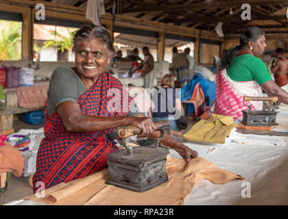 Ein Lächeln glücklich indische Frau Bügeln bei Dhobi khana öffentliche Wäscherei in Fort Kochi mit einem traditionellen alten Eisen. Stockfoto