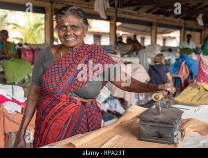 Ein Lächeln glücklich indische Frau Bügeln bei Dhobi khana öffentliche Wäscherei in Fort Kochi mit einem traditionellen alten Eisen. Stockfoto