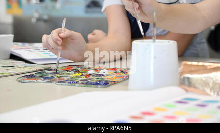 Nahaufnahme der Student Hände in Bildende Kunst Klasse mit einem Pinsel Eintauchen in hellen Farben auf einer Farbpalette. Kreative bildende Kunst praktisch. Stockfoto