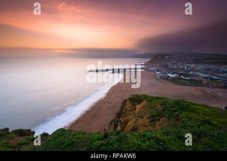 West Bay, Dorset, Großbritannien. 21. Februar 2019. UK Wetter. Sonnenuntergang an der West Bay auf der Dorset Jurassic Coast mit niedrigen Wolken und Nebel auf die Felsen in der Ferne. Foto: Graham Jagd-/Alamy leben Nachrichten Stockfoto