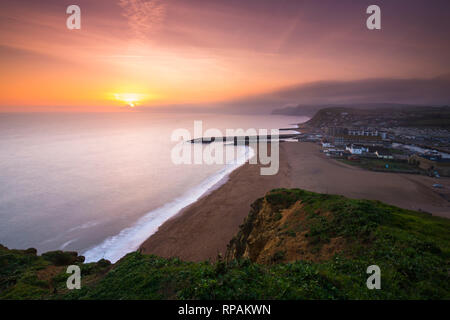 West Bay, Dorset, Großbritannien. 21. Februar 2019. UK Wetter. Sonnenuntergang an der West Bay auf der Dorset Jurassic Coast mit niedrigen Wolken und Nebel auf die Felsen in der Ferne. Foto: Graham Jagd-/Alamy leben Nachrichten Stockfoto