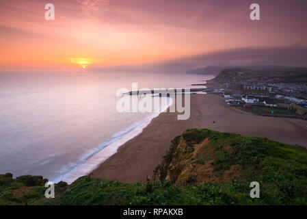 West Bay, Dorset, Großbritannien. 21. Februar 2019. UK Wetter. Sonnenuntergang an der West Bay auf der Dorset Jurassic Coast mit niedrigen Wolken und Nebel auf die Felsen in der Ferne. Foto: Graham Jagd-/Alamy leben Nachrichten Stockfoto