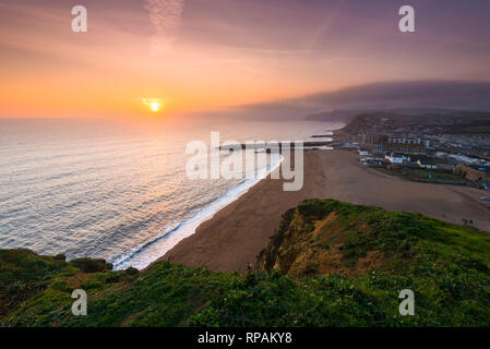 West Bay, Dorset, Großbritannien. 21. Februar 2019. UK Wetter. Sonnenuntergang an der West Bay auf der Dorset Jurassic Coast mit niedrigen Wolken und Nebel auf die Felsen in der Ferne. Foto: Graham Jagd-/Alamy leben Nachrichten Stockfoto