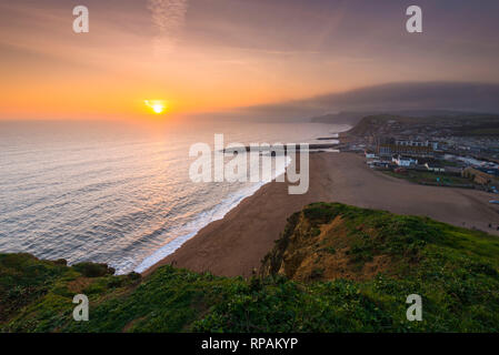 West Bay, Dorset, Großbritannien. 21. Februar 2019. UK Wetter. Sonnenuntergang an der West Bay auf der Dorset Jurassic Coast mit niedrigen Wolken und Nebel auf die Felsen in der Ferne. Foto: Graham Jagd-/Alamy leben Nachrichten Stockfoto