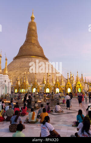 Die Gläubigen sitzen auf dem Boden vor der goldenen Kuppel der Shwedagon Pagode in der Abenddämmerung. Kerzen Stupas, dass House ein Buddha Statue beleuchten. Stockfoto