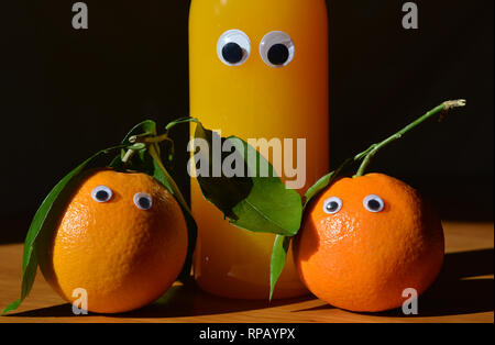 Kreative spaß essen Fotografie. Zwei frische Orangen mit kulleraugen und ein googly eyed Flasche frisch gepressten Orangensaft. Stockfoto