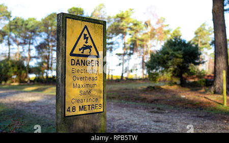 Warnschild auf die Gefahr der Overhead für die Stromversorgung Zeilen über Wander- und Radwege im New Forest Hampshire England. Stockfoto