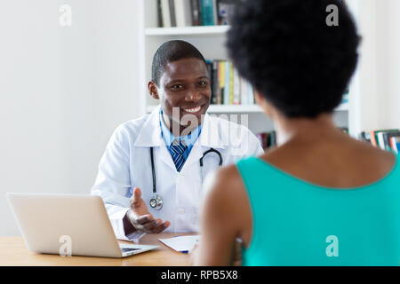 Afrikanische amerikanische Arzt mit guten Nachrichten für weibliche Patienten im Krankenhaus Stockfoto