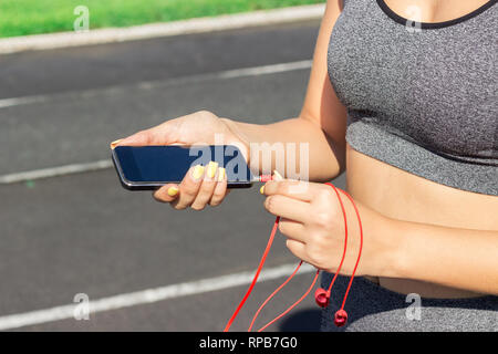 Runner girl Holding Smartphone und fügt Kopfhörer mit dem Telefon. Training am Morgen Zeit. Menschen Sport und Fitness Concept. Stockfoto