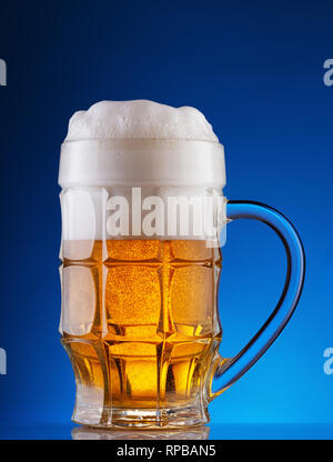 Facettierte Tasse helles Bier mit Schaum auf blauem Hintergrund Stockfoto