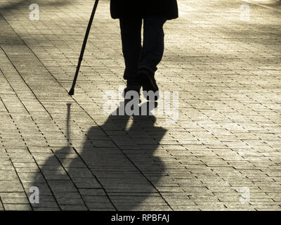 Silhouette der Mann mit einem Stock, lange Schatten auf Pflaster. Konzept der blinden Person, hinkend, Behinderung, Alter, Erkrankungen der Wirbelsäule Stockfoto