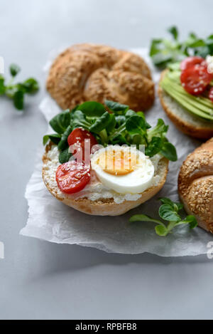 Bagel Sandwiches mit Frischkäse, Avocado, Tomate, Ei und Grüns auf grau Holz- Hintergrund. Selektive konzentrieren. Gesunde Ernährung oder vegetarisches Essen co Stockfoto