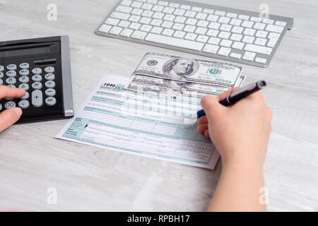 Sicht Foto von Frau Berechnung und füllen uns Steuerformular neben Computer Tastatur, Dollar, Rechnungen und Steuern Form 1040. 15. April 2019 Steuer Tag Stockfoto