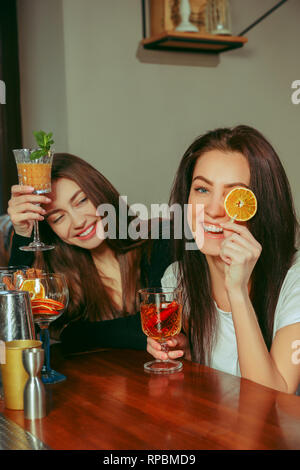 Weibliche Freunde haben eines Drinks an der Bar. Sie sitzen an einem Holztisch mit Cocktails. Sie sind anstoßen Stockfoto