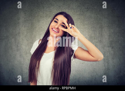 Porträt einer glückliche junge Frau, die einen Frieden Geste auf grauem Hintergrund. Stockfoto