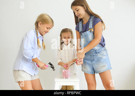 Kinder mit Schraubendreher, Zange und Hammer durch den Pink Pig piggy Bank auf weißem Hintergrund Stockfoto