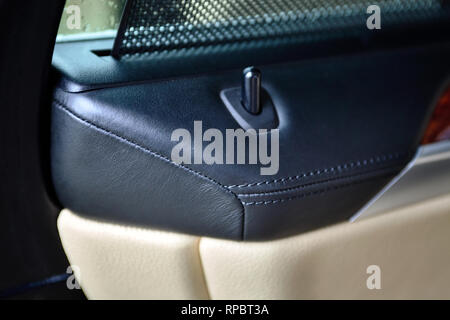 Close-up Luxus genäht Leder exklusives Interieur in schwarz und beige Farben eines Luxuswagens mit einem Verriegelungsknopf an der Innenseite der Autotür. Stockfoto