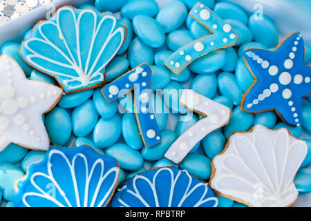 Weiße Muschel Platte voller Pralinen mit blauer Zuckerglasur, Cookies wie Muscheln, Sterne und Nummer Sieben und viele kleine Gläser mit Marshmallow auf t Stockfoto