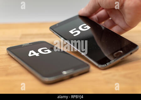 Zwei Handys auf einem Schreibtisch aus Holz. Hand wählt das Telefon mit dem Etikett "5 G" anstelle des "4G". Stockfoto